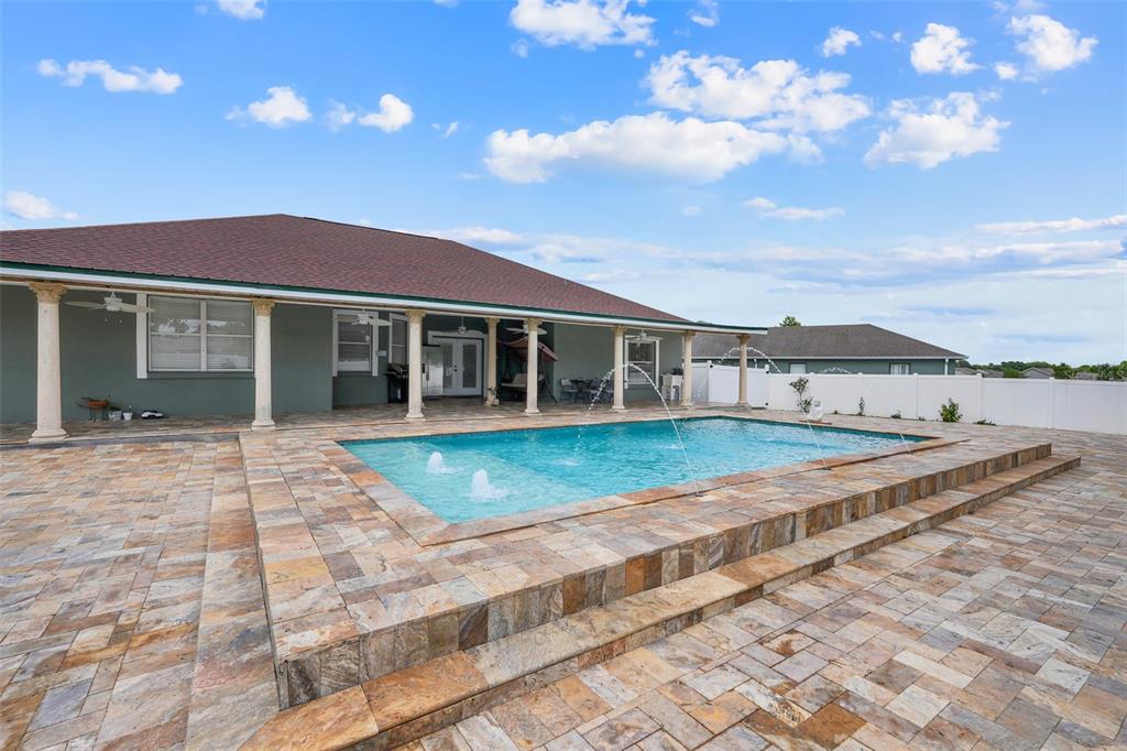 A backyard features a raised swimming pool with fountains and a stone paver patio — 2735 BERKFORD CIRCLE, LAKELAND, FL