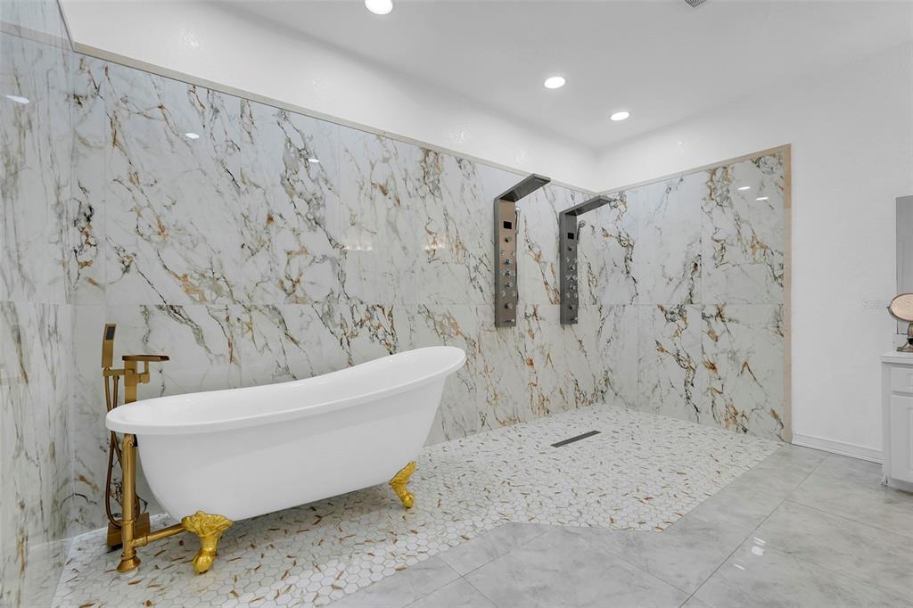 A bathroom features a white freestanding tub, a walk-in shower, and marble-patterned wall tiles — 2735 BERKFORD CIRCLE, LAKELAND, FL