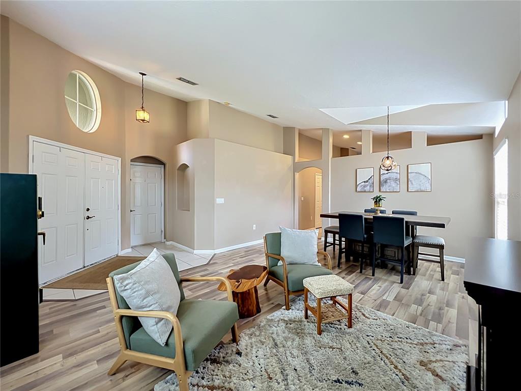 A living and dining area features wood-look flooring, vaulted ceilings, and two green armchairs — 2886 SWEETSPIRE CIRCLE, OVIEDO, FL