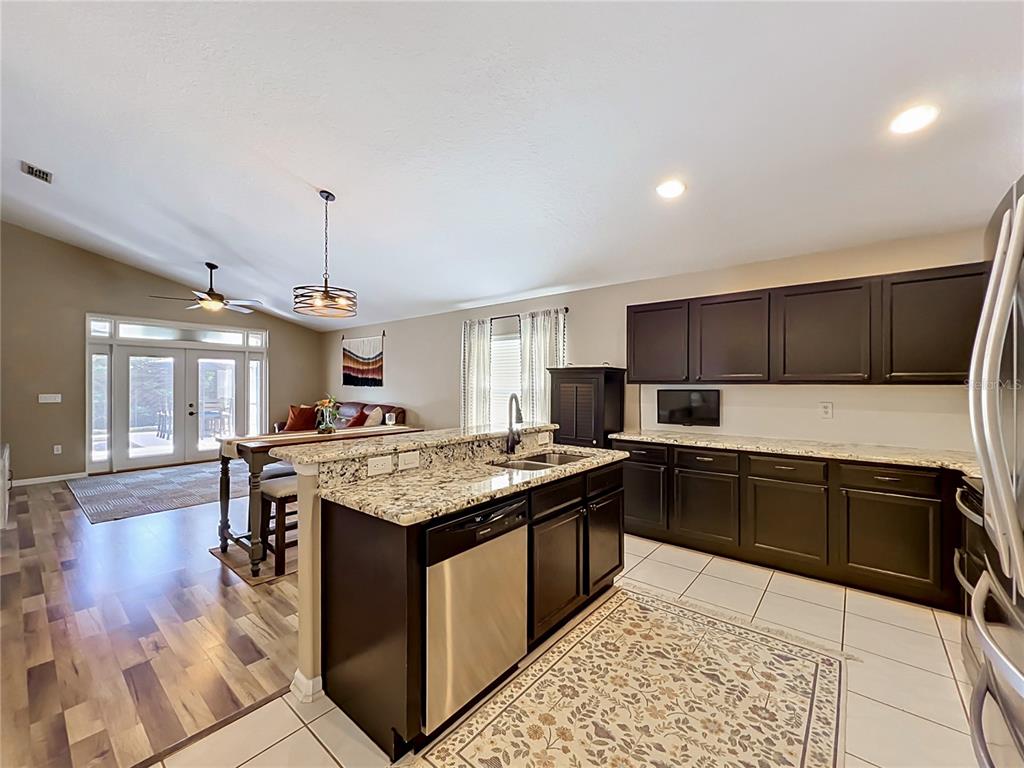 A kitchen with dark cabinets and granite countertops opens into a dining and living area — 2886 SWEETSPIRE CIRCLE, OVIEDO, FL