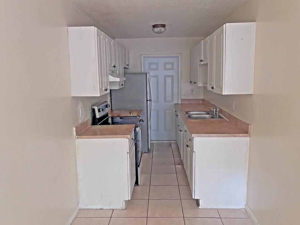 A galley kitchen features white cabinets, tan laminate countertops, tile flooring, and stainless steel appliances — 2620 Riverland Drive # 2, Fort Lauderdale FL 33312, FORT LAUDERDALE, FL