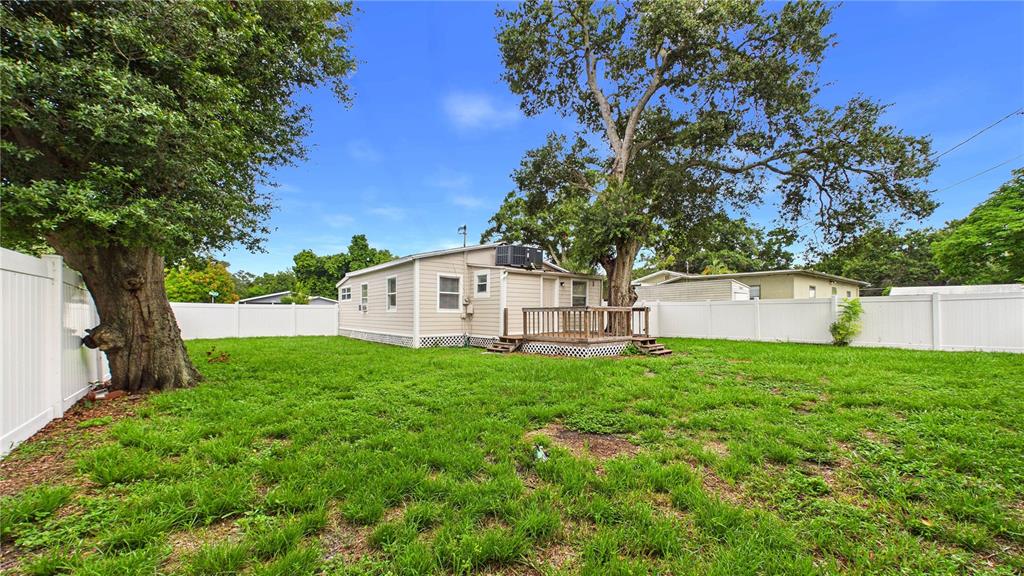 A backyard with a small house, a wooden deck, and large trees enclosed by white fencing — 5001 RENA STREET N, ST PETERSBURG, FL