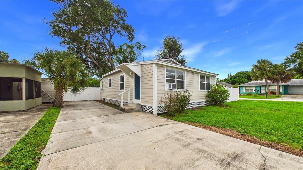 A light-colored single-story house with a concrete driveway, a palm tree, and a fenced yard — 5001 RENA STREET N, ST PETERSBURG, FL