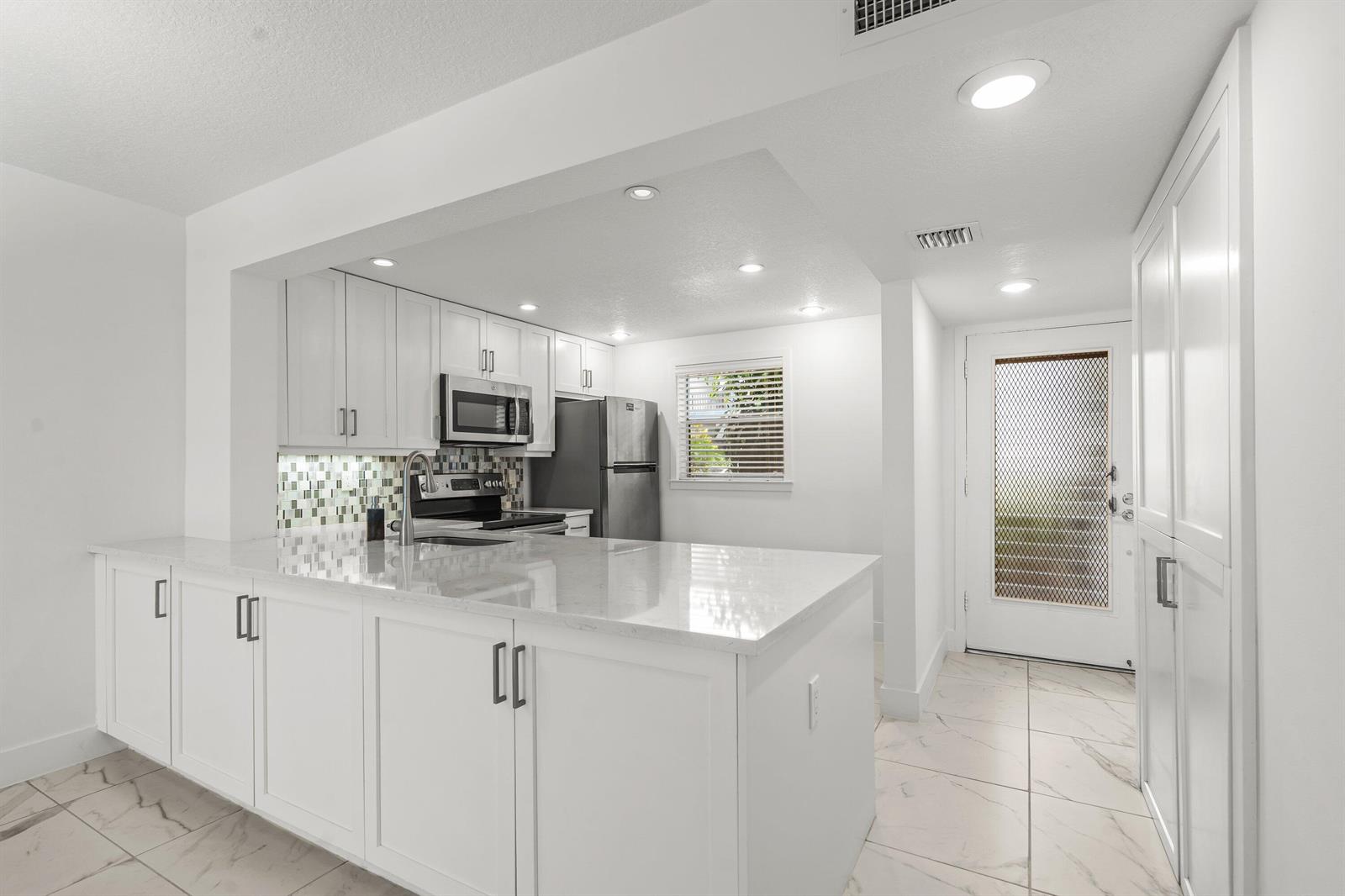 A bright kitchen features white cabinetry, quartz countertops, a mosaic backsplash, and marble-look tile flooring — 3090 Holiday Springs Boulevard Unit 109, Margate FL 33063, MARGATE, FL