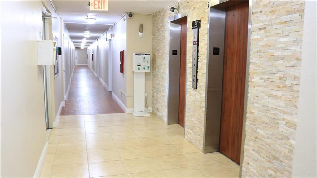 A hallway with tiled floors leads to two elevators with wood-look doors and stone walls — 7300 NW 17th Street # 202, Plantation FL 33313, PLANTATION, FL