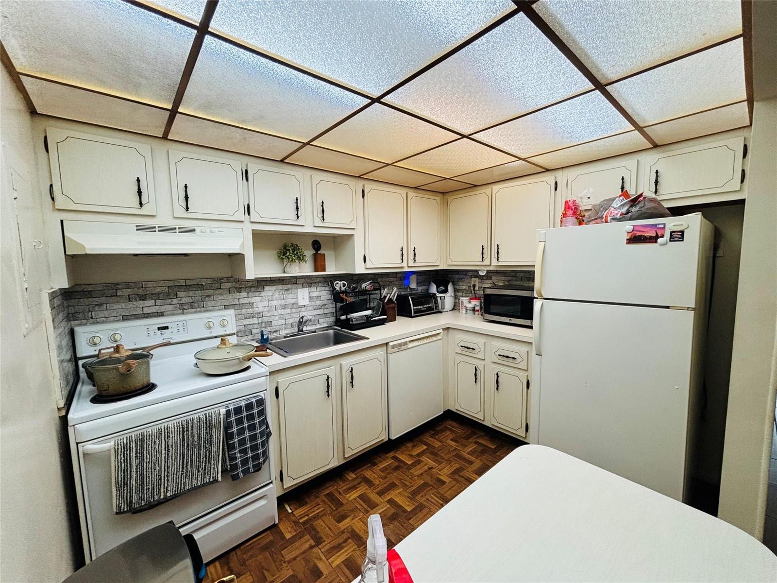 A kitchen features white cabinets, a drop ceiling with grid lighting, and parquet wood flooring — 7300 NW 17th Street # 202, Plantation FL 33313, PLANTATION, FL