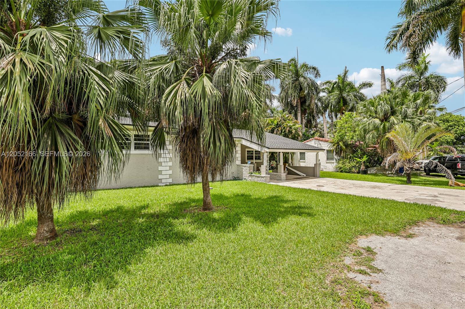 A single-story house with a carport and palm trees sits on a grassy lot — 130 NW 85th St, Miami FL 33150, MIAMI, FL