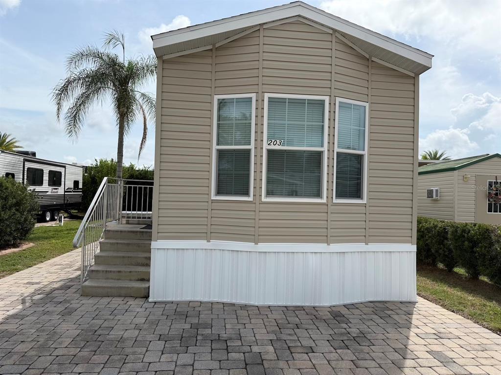 A tan manufactured home with white skirting and a paver patio sits under a palm tree — 2414 LIMEWOOD AVENUE, CLERMONT, FL