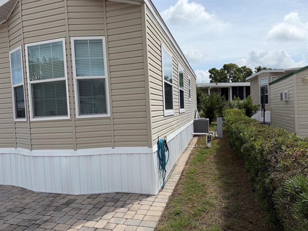 The exterior of a tan manufactured home features white skirting and a paved driveway — 2414 LIMEWOOD AVENUE, CLERMONT, FL