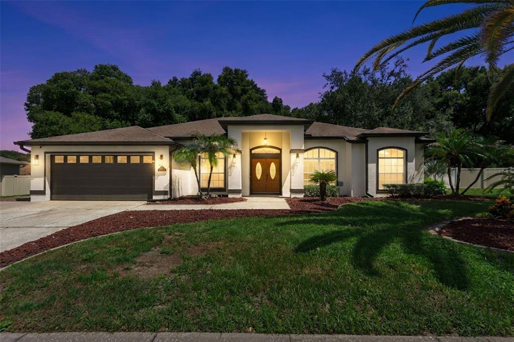 A single-story house with a two-car garage, arched windows, and a central entryway at dusk — 16413 ARROWHEAD TRL, CLERMONT, FL
