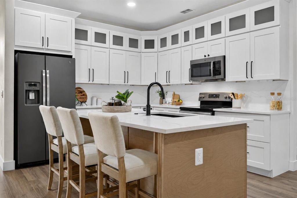 A modern kitchen features white cabinetry, a wood-toned island, and a black refrigerator — 16413 ARROWHEAD TRL, CLERMONT, FL
