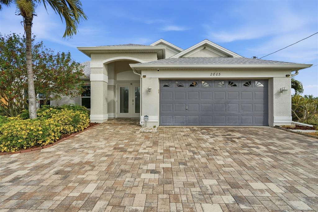 A single-story house features a gray garage, a paved driveway, and a palm tree — 2803 SW 34TH TERRACE, CAPE CORAL, FL