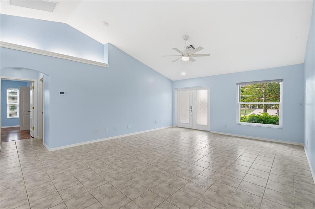 A spacious, light blue living room features vaulted ceilings, tile flooring, and glass patio doors — 2803 SW 34TH TERRACE, CAPE CORAL, FL