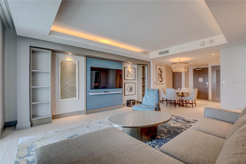A modern living room features a blue accent wall, a television, and a dining area — 691 S GULFVIEW BOULEVARD UNIT 1608, CLEARWATER BEACH, FL