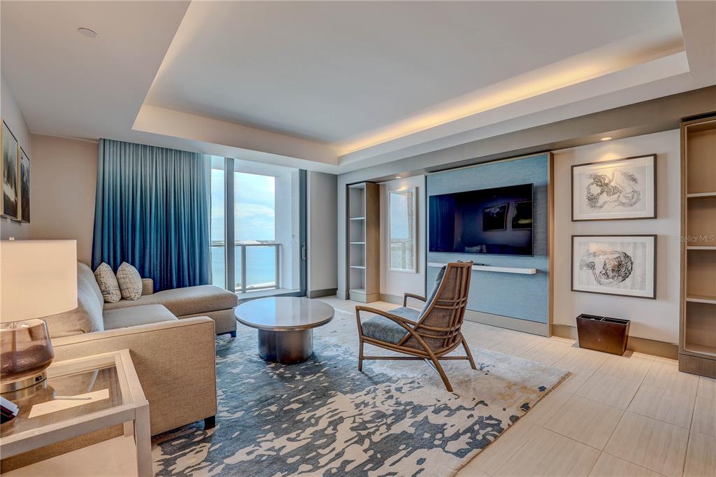 A modern living room features a sectional sofa, a lounge chair, and a wall-mounted television — 691 S GULFVIEW BOULEVARD UNIT 1608, CLEARWATER BEACH, FL