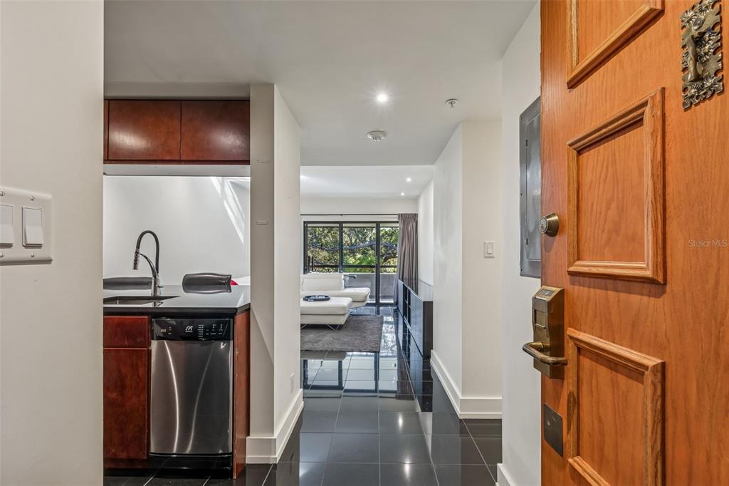 An entryway leads past a kitchen with dark cabinets into a living room with balcony access — 36750 US HIGHWAY 19 N UNIT 19306, PALM HARBOR, FL