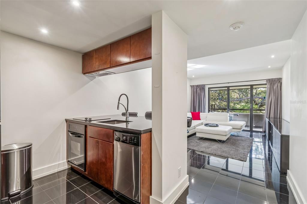 A kitchen with dark wood cabinets and black countertops opens into a bright living room — 36750 US HIGHWAY 19 N UNIT 19306, PALM HARBOR, FL