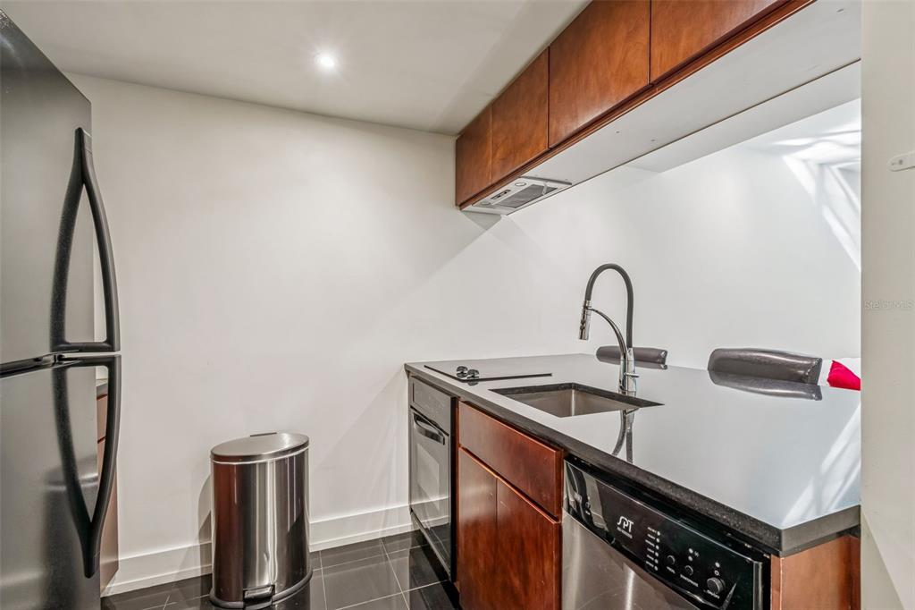 A kitchen with dark wood cabinets, black countertops, stainless steel appliances, and black tile flooring — 36750 US HIGHWAY 19 N UNIT 19306, PALM HARBOR, FL