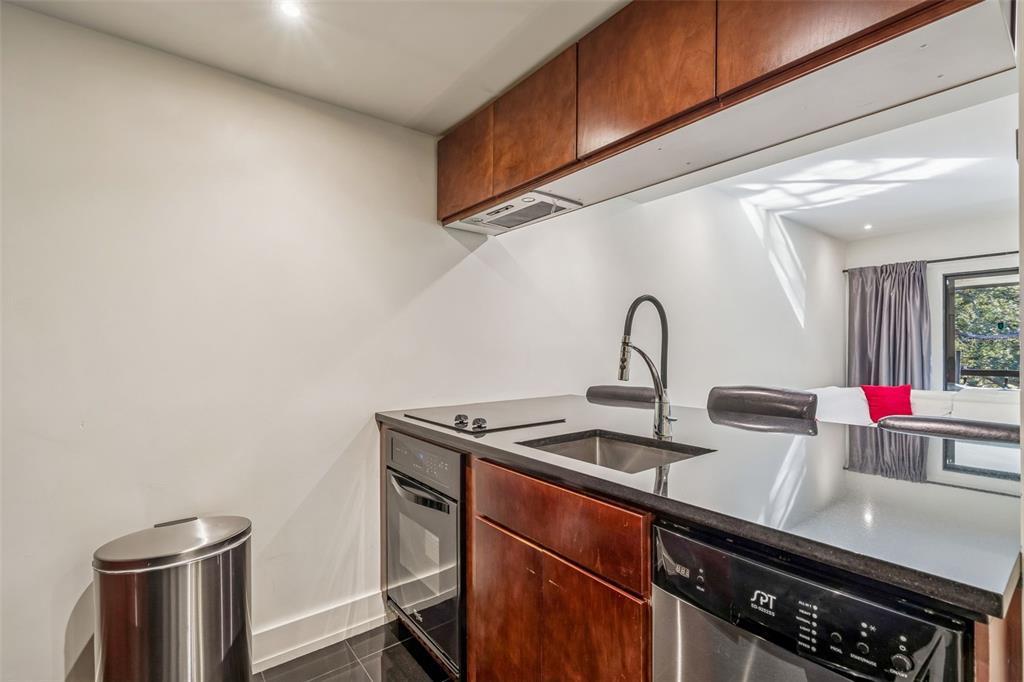 A compact kitchen features dark wood cabinets, black countertops, stainless steel appliances, and a sink — 36750 US HIGHWAY 19 N UNIT 19306, PALM HARBOR, FL