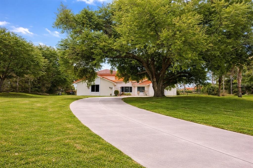 A white house with a terracotta roof sits at the end of a curved concrete driveway — 12624 LAKE DENISE BOULEVARD, CLERMONT, FL