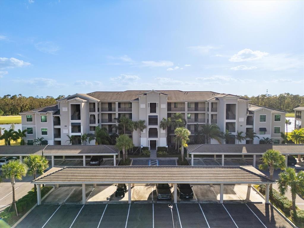 An exterior view of a multi-story apartment building with covered parking spaces in the foreground — 17704 GAWTHROP DRIVE UNIT 207, BRADENTON, FL