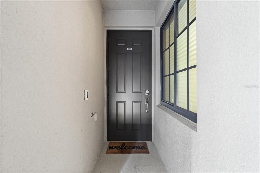 A dark gray front door with a welcome mat sits in a small entryway — 17704 GAWTHROP DRIVE UNIT 207, BRADENTON, FL
