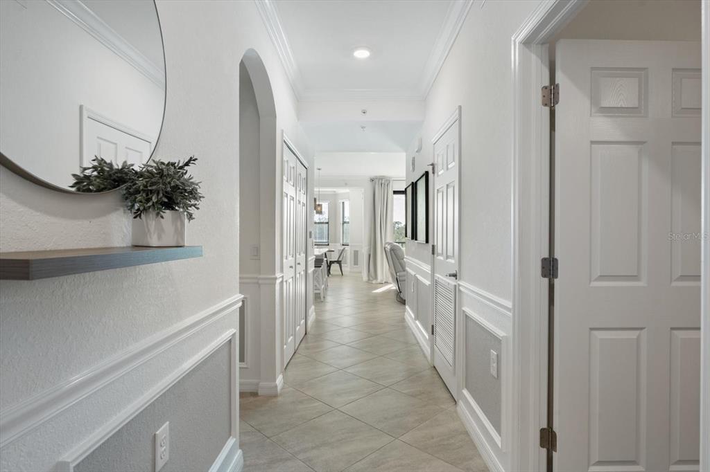 A bright hallway with white wainscoting, tile flooring, and a mirror leads to a living area — 17704 GAWTHROP DRIVE UNIT 207, BRADENTON, FL