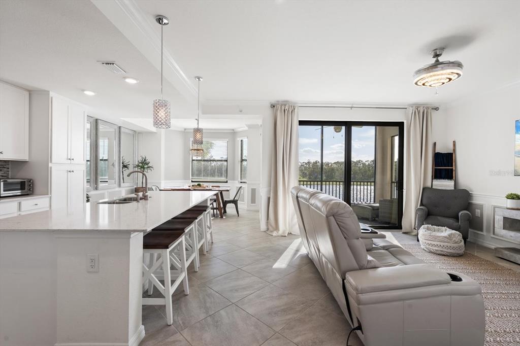 An open-concept kitchen and living area features white cabinetry, a breakfast bar, and sliding doors — 17704 GAWTHROP DRIVE UNIT 207, BRADENTON, FL