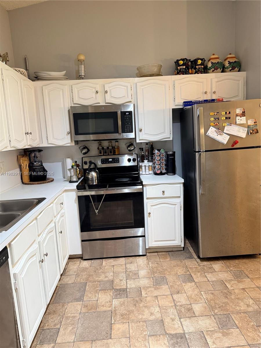 A kitchen features white cabinetry, stainless steel appliances, and tiled flooring — 9963 Baywater Dr, Boca Raton FL 33496, BOCA RATON, FL