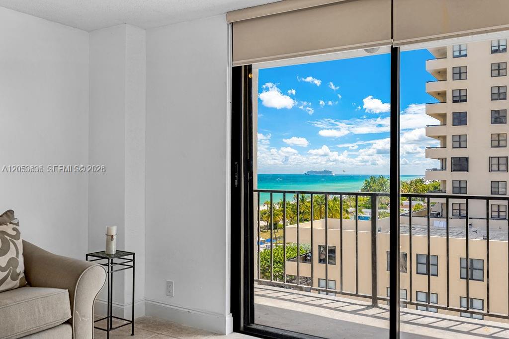 A living room with a beige sofa and a balcony overlooking the ocean and buildings — 2625 Collins Ave # 702, Miami Beach FL 33140, MIAMI BEACH, FL