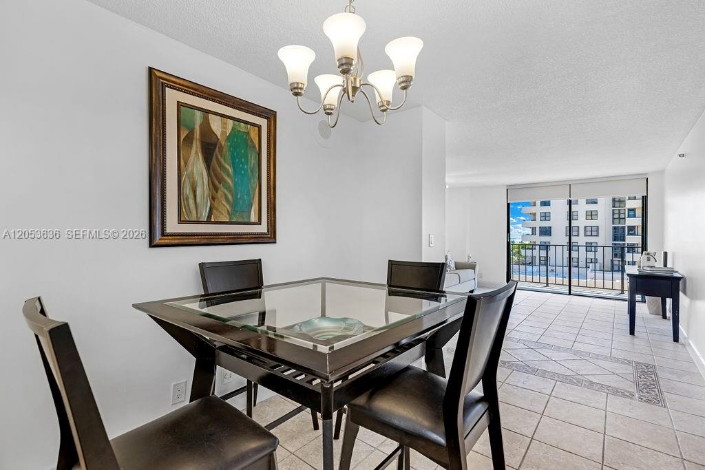A dining area features a glass-topped table, dark chairs, a chandelier, and a balcony view — 2625 Collins Ave # 702, Miami Beach FL 33140, MIAMI BEACH, FL