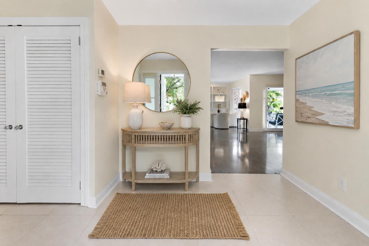 A bright entryway features a wooden console table, a round mirror, and a woven rug — 3240 Lakeview Drive, Pompano Beach FL 33062, POMPANO BEACH, FL