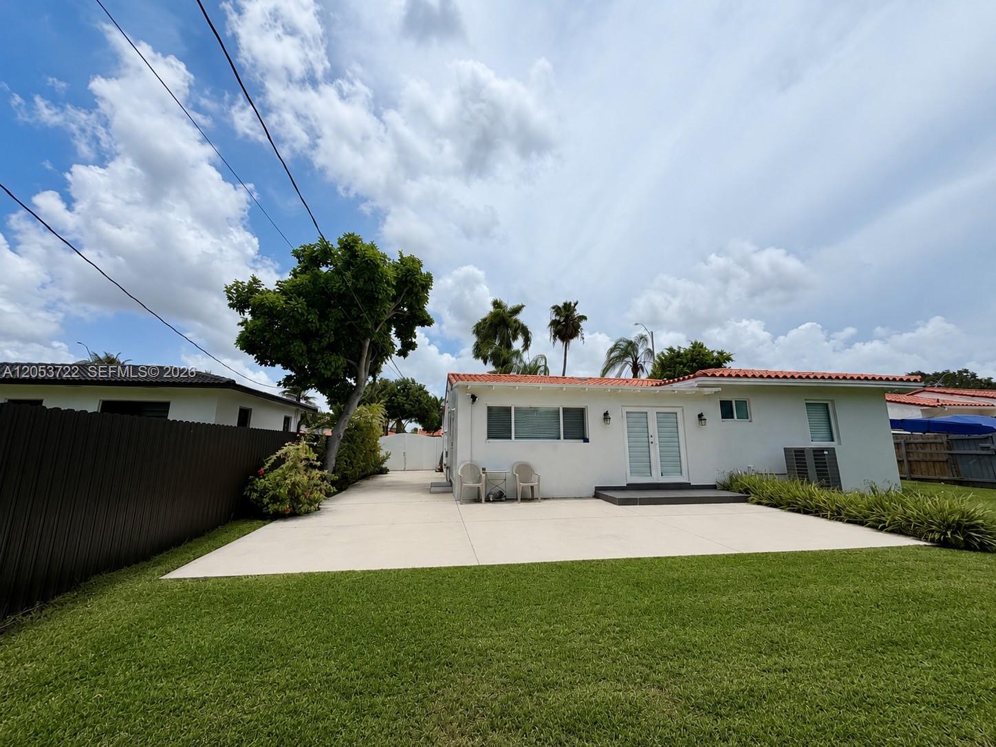 The exterior of a white house features a concrete patio, lawn, and palm trees — 6320 SW 24th St, Miami FL 33155, MIAMI, FL