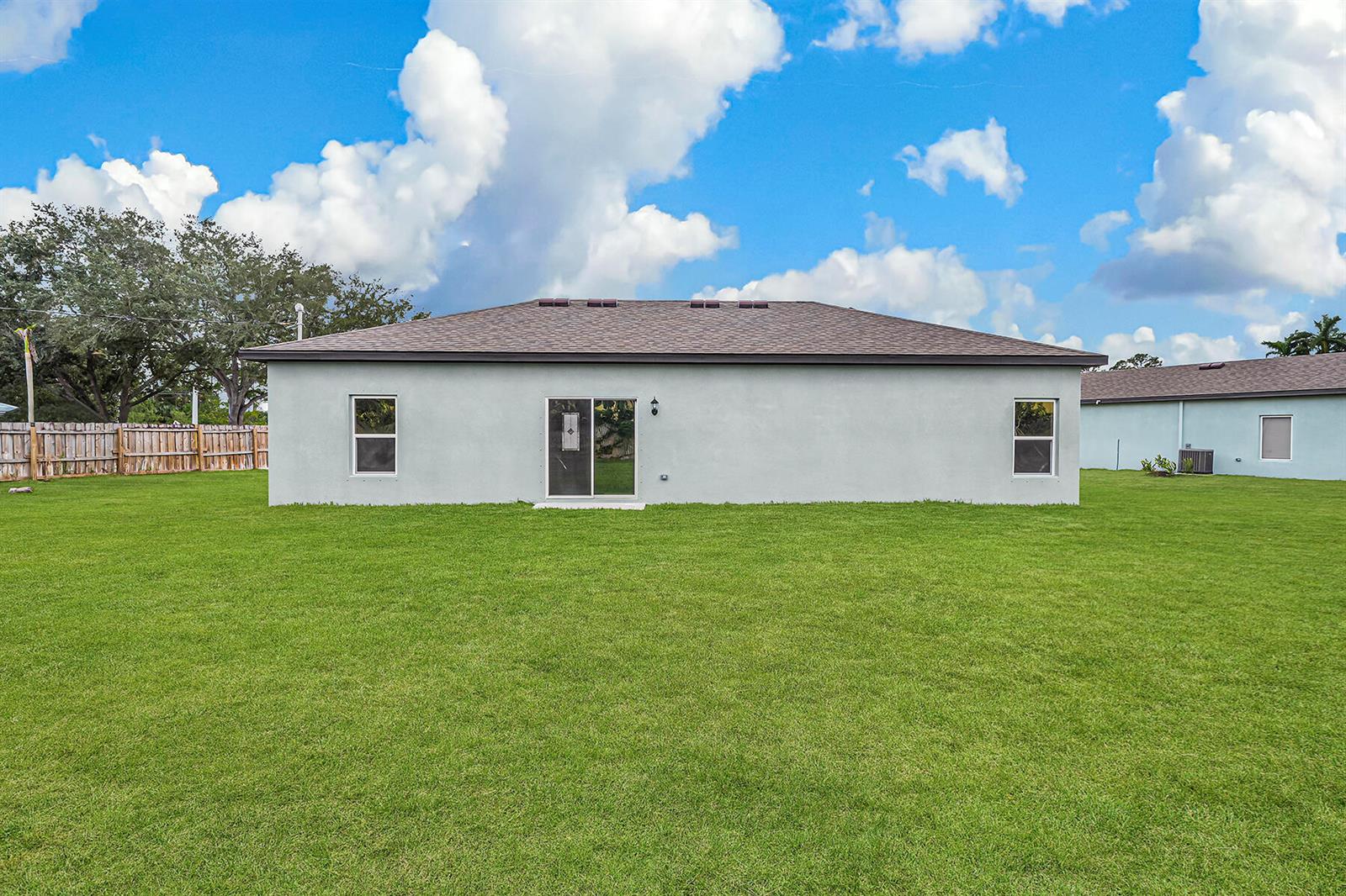 The back exterior of a single-story house features a large lawn and sliding glass doors — 1613 SE Grapeland Avenue, Port St. Lucie FL 34952, PORT ST. LUCIE, FL