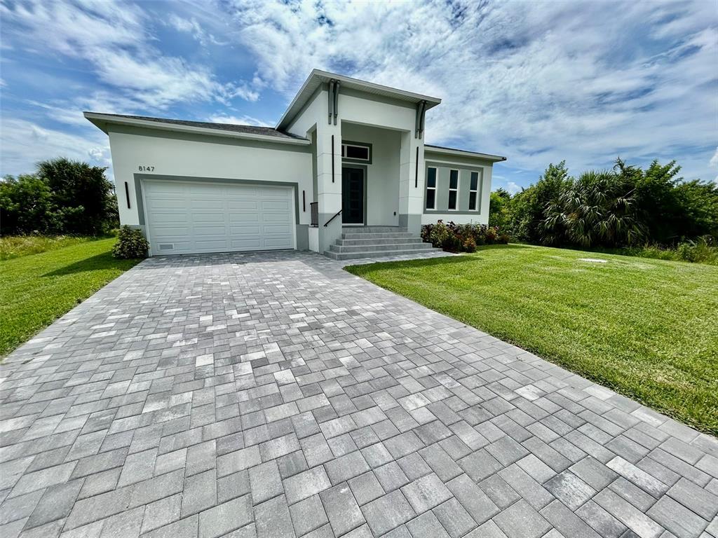 A modern single-story house features a white exterior, a paved driveway, and a covered entryway — 8147 TRACY CIRCLE, PORT CHARLOTTE, FL