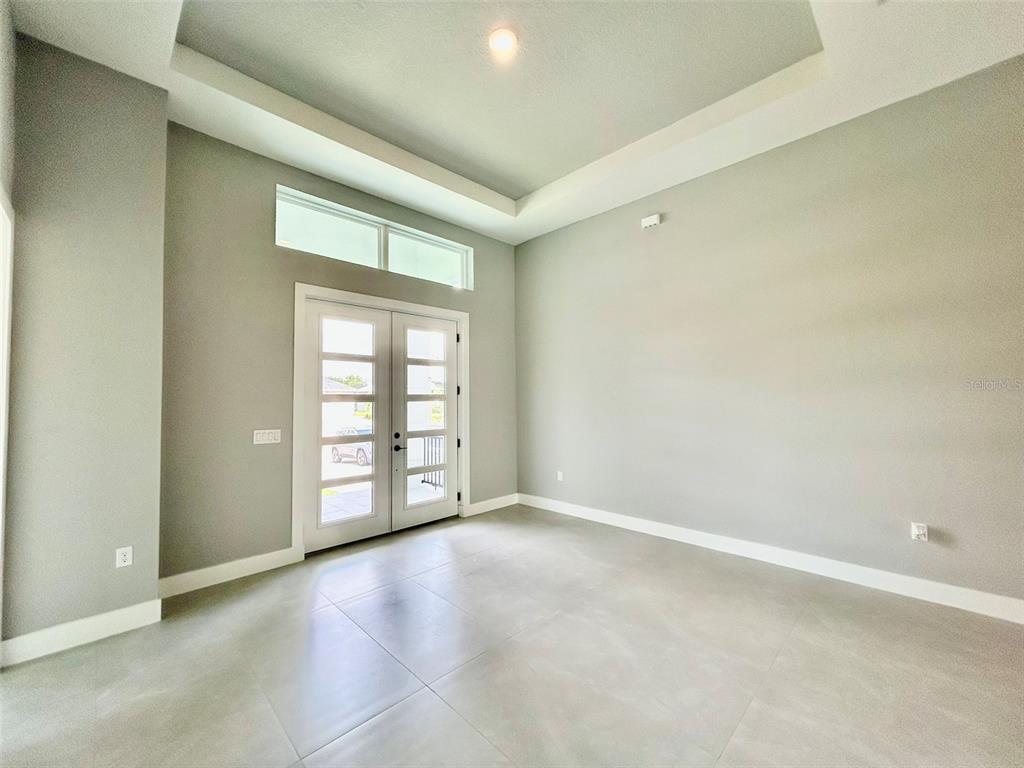 An empty room features light gray walls, large floor tiles, and double glass-paneled entry doors — 8147 TRACY CIRCLE, PORT CHARLOTTE, FL