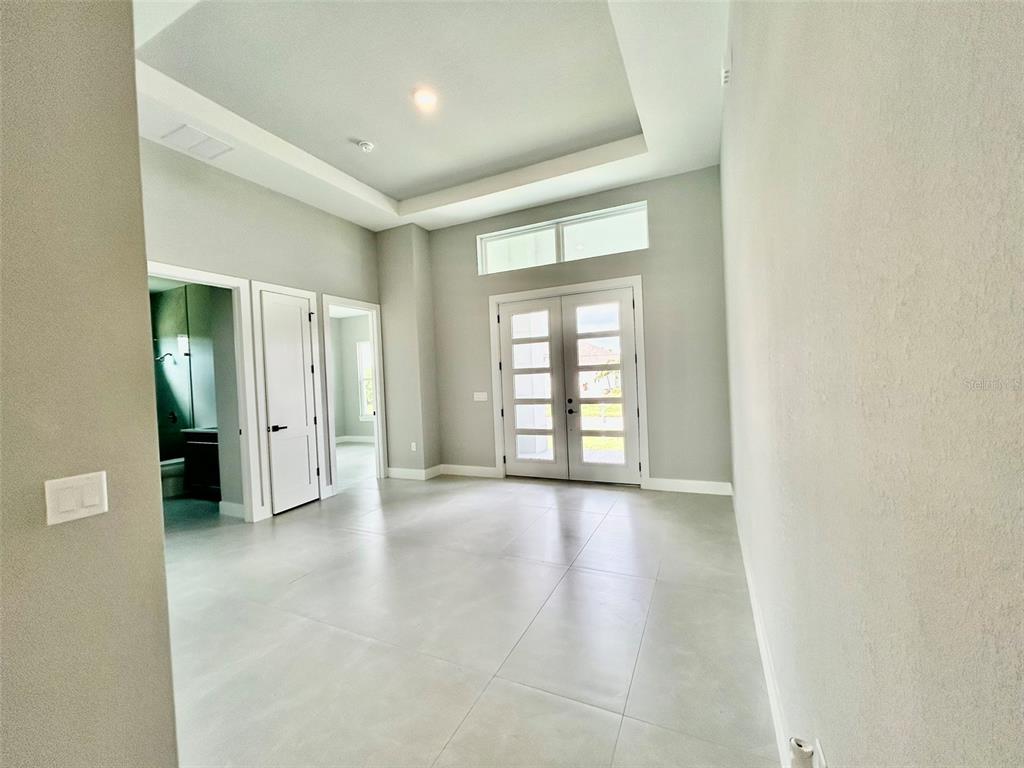 A bright, modern entryway features a tray ceiling, large tile flooring, and double glass doors — 8147 TRACY CIRCLE, PORT CHARLOTTE, FL