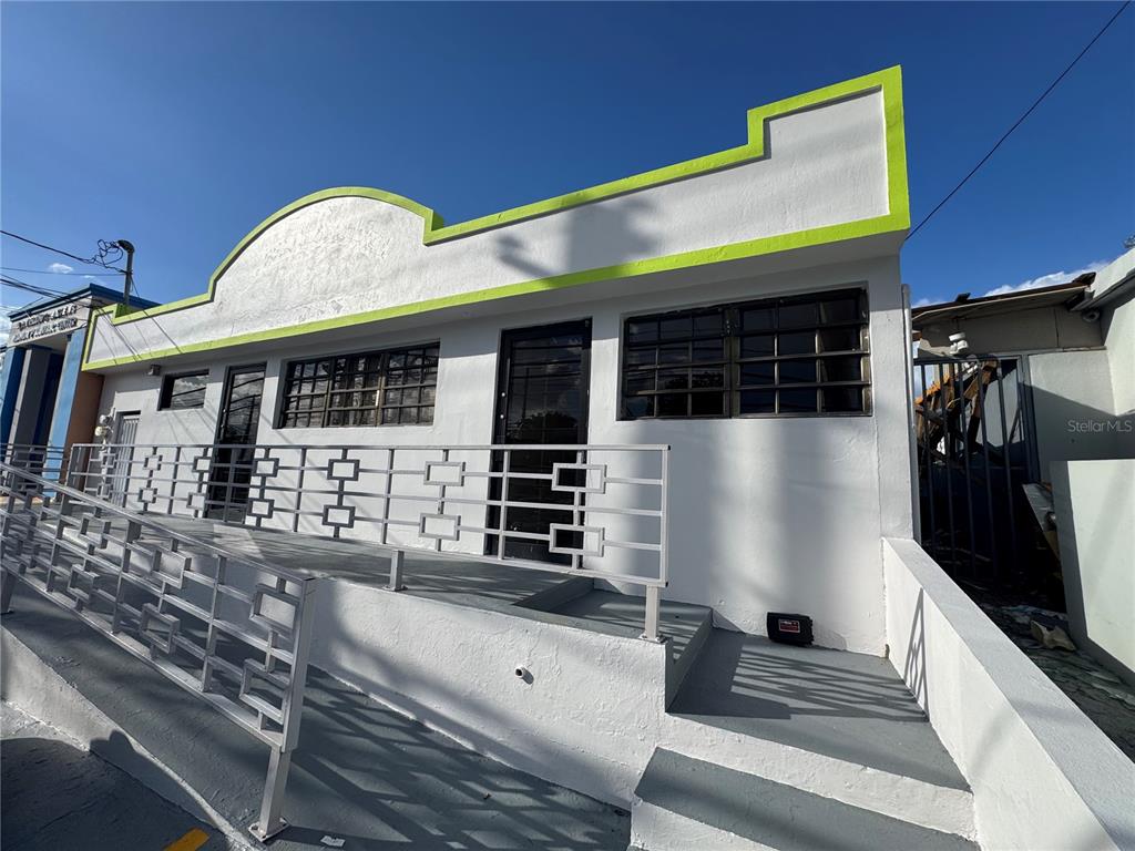 A white commercial building exterior features a wheelchair ramp, metal railings, and lime green trim — MARGINAL ELIOT VELEZ ST. ATENAS UNIT J-14, MANATI, PR