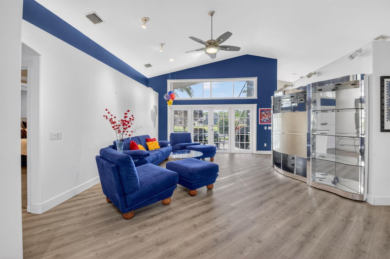 A living room features blue furniture, wood-look flooring, a vaulted ceiling, and glass display cabinets — 7528 Tarpon Cove Circle, Lake Worth FL 33467, LAKE WORTH, FL