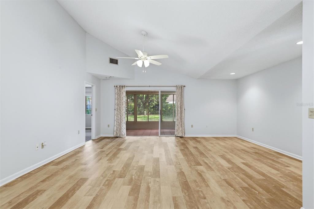 A spacious living room with light wood-look flooring, vaulted ceilings, and sliding glass patio doors — 6420 CARRINGTON CIRCLE UNIT 35, SARASOTA, FL