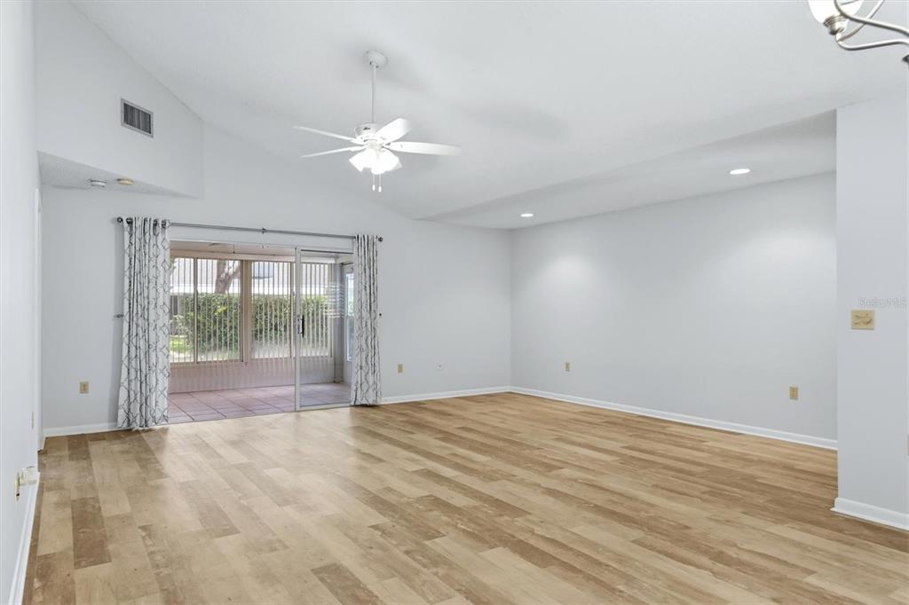 A bright living room features light wood-look flooring, a vaulted ceiling, and sliding glass doors — 6420 CARRINGTON CIRCLE UNIT 35, SARASOTA, FL