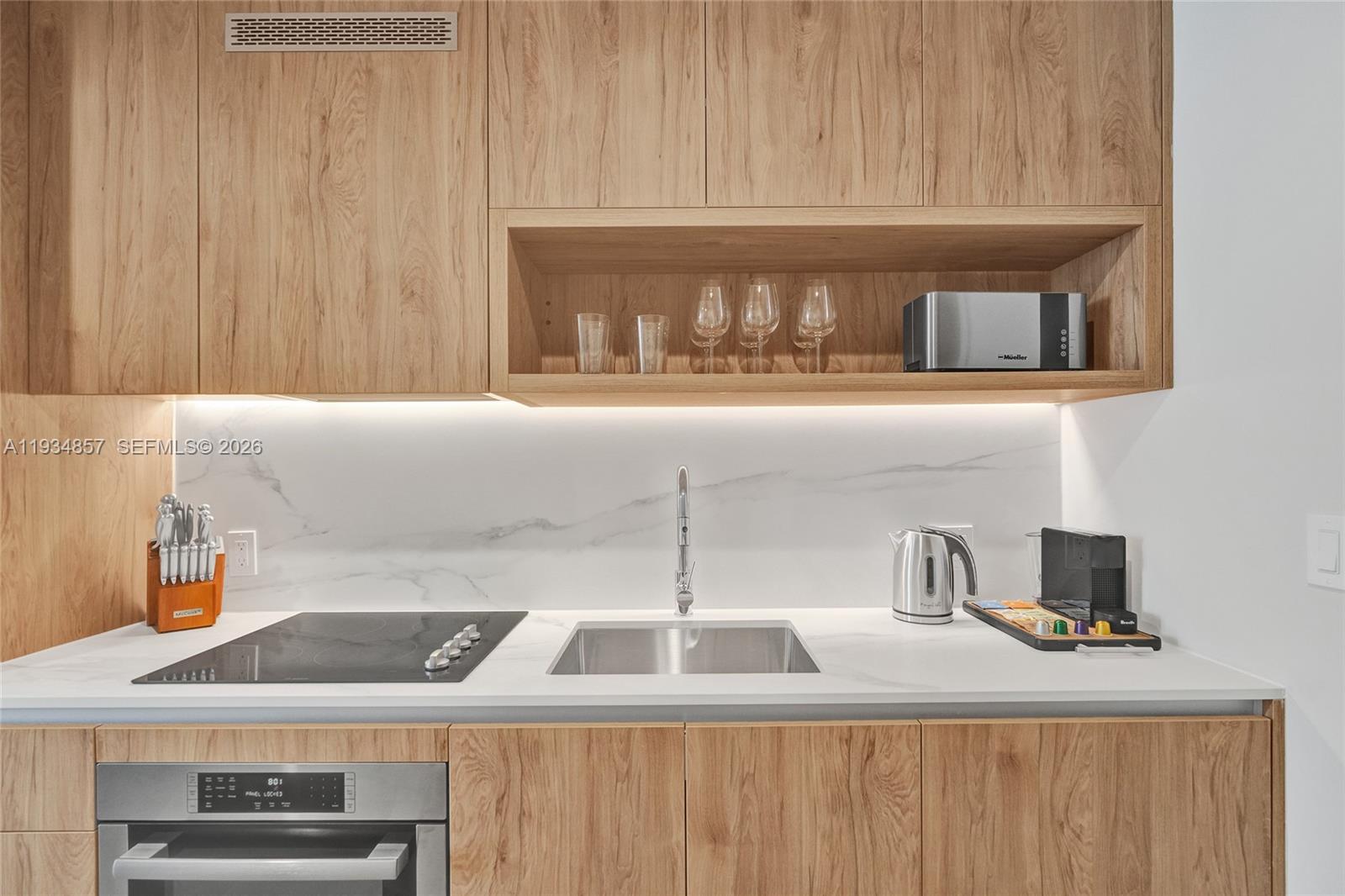 A modern kitchen features wood cabinetry, a white marble backsplash, and stainless steel appliances — 11 NE 6TH # 2013, Miami FL 33132, MIAMI, FL