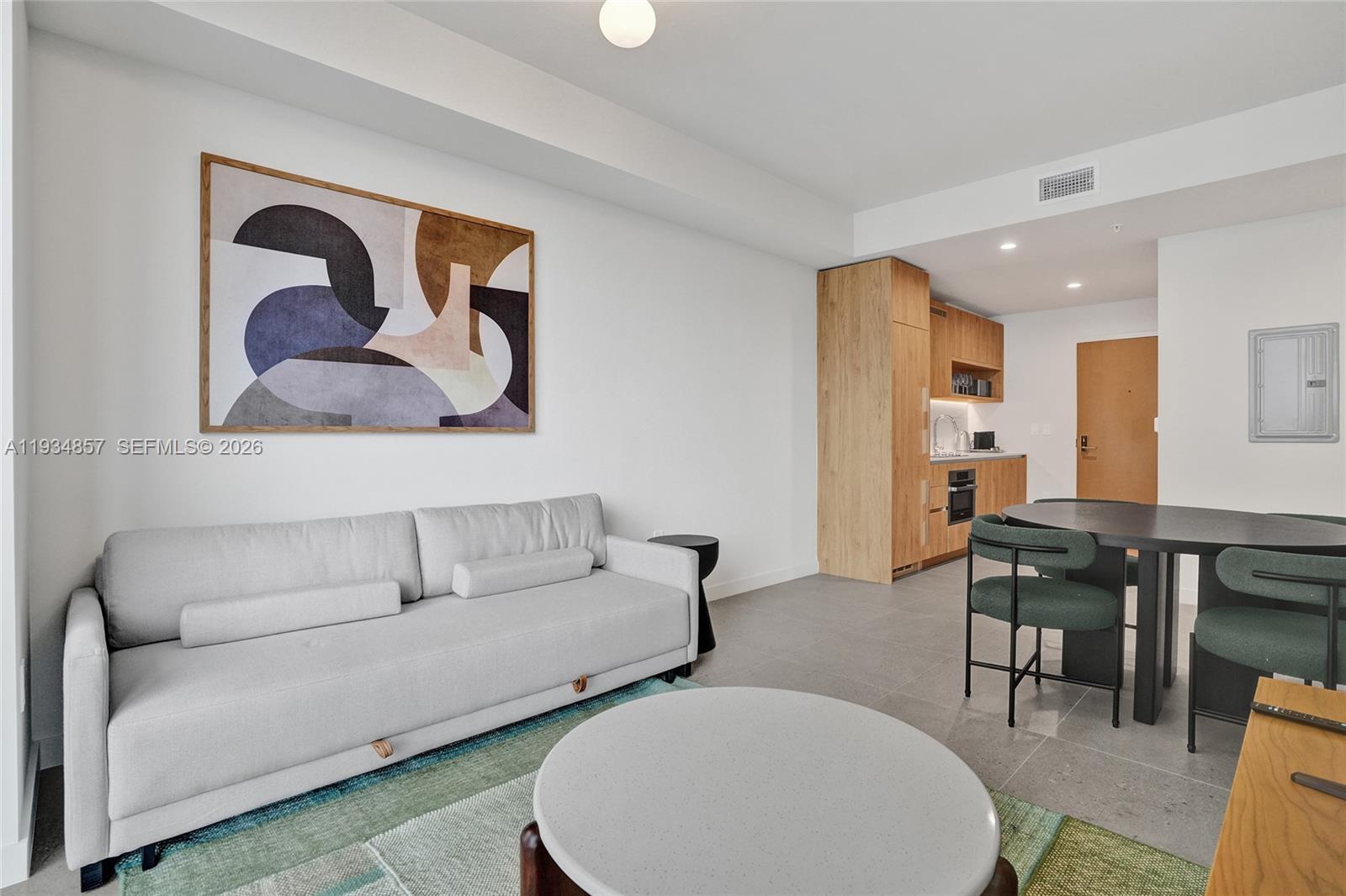 A modern living room features a light gray sofa, circular coffee table, and adjacent kitchenette — 11 NE 6TH # 2013, Miami FL 33132, MIAMI, FL