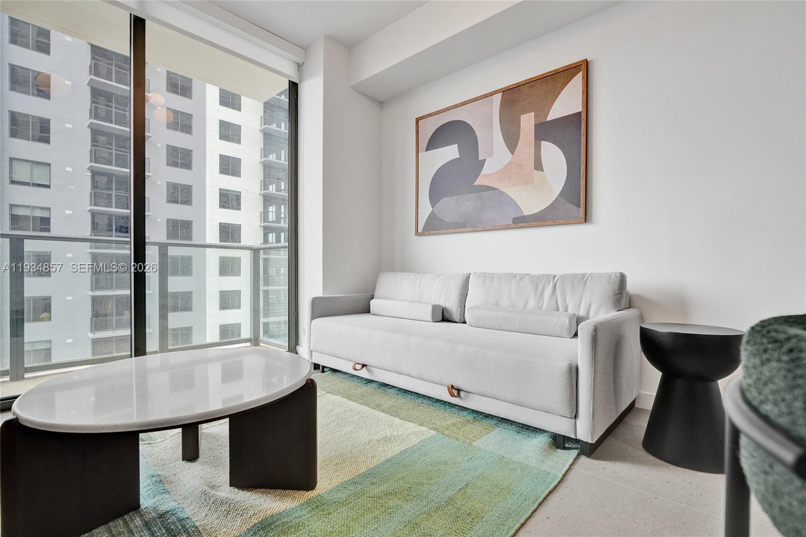 A modern living room features a light gray sofa, a patterned rug, and a balcony view — 11 NE 6TH # 2013, Miami FL 33132, MIAMI, FL