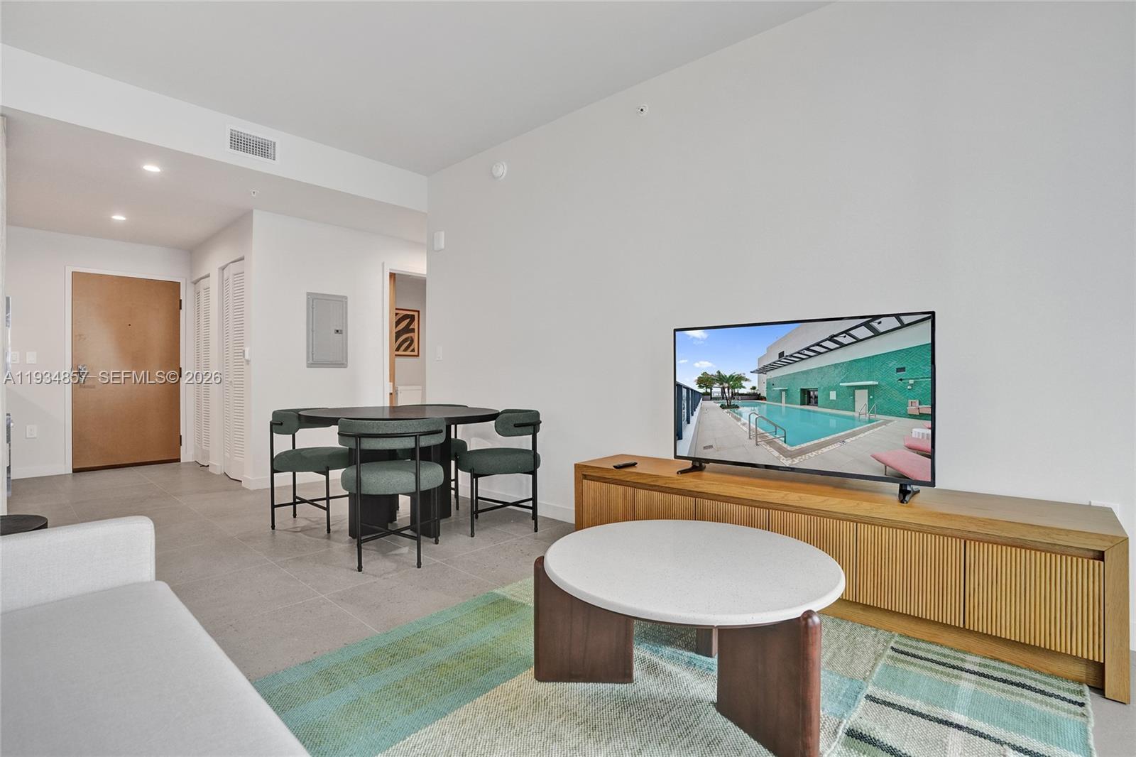 A living room features a television on a wooden console, a round coffee table, and a dining set — 11 NE 6TH # 2013, Miami FL 33132, MIAMI, FL