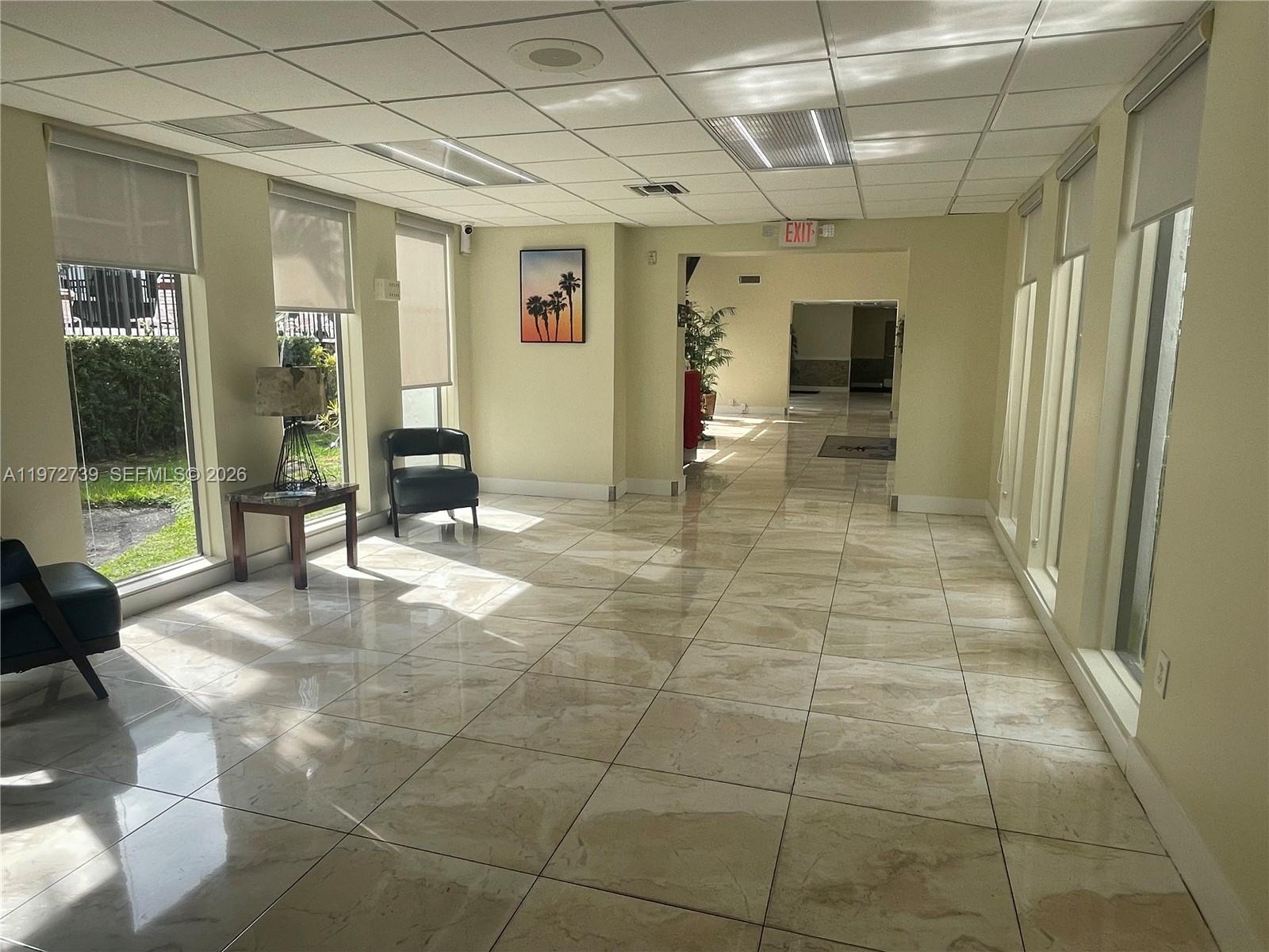 A bright lobby features large windows, tiled floors, and a hallway leading to an exit — 201 178th Dr # 334, Sunny Isles Beach FL 33160, SUNNY ISLES BEACH, FL