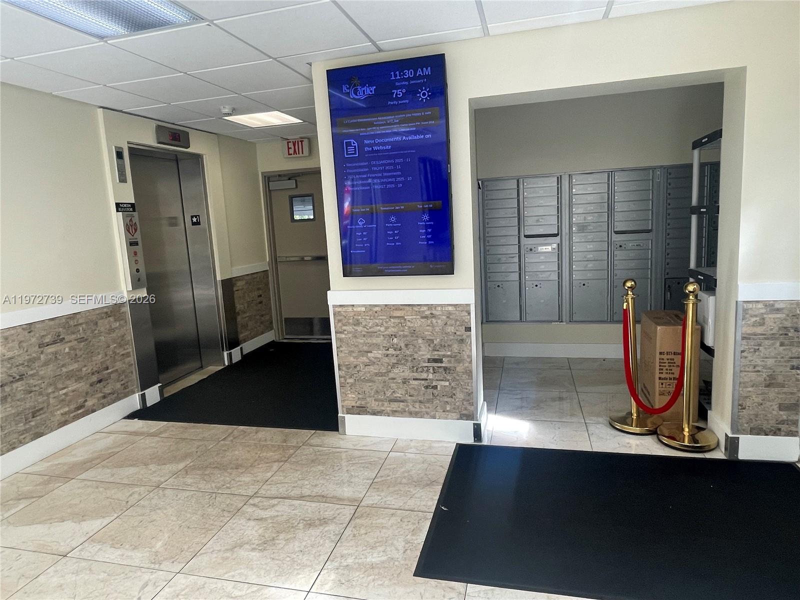 A building lobby features an elevator, a digital information screen, and a wall of mailboxes — 201 178th Dr # 334, Sunny Isles Beach FL 33160, SUNNY ISLES BEACH, FL