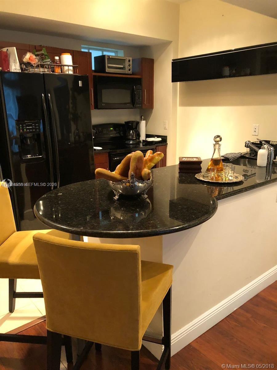 A kitchen features a black refrigerator, dark granite countertops, and yellow bar stools — 7290 SW 90th St # 303, Miami FL 33156, MIAMI, FL