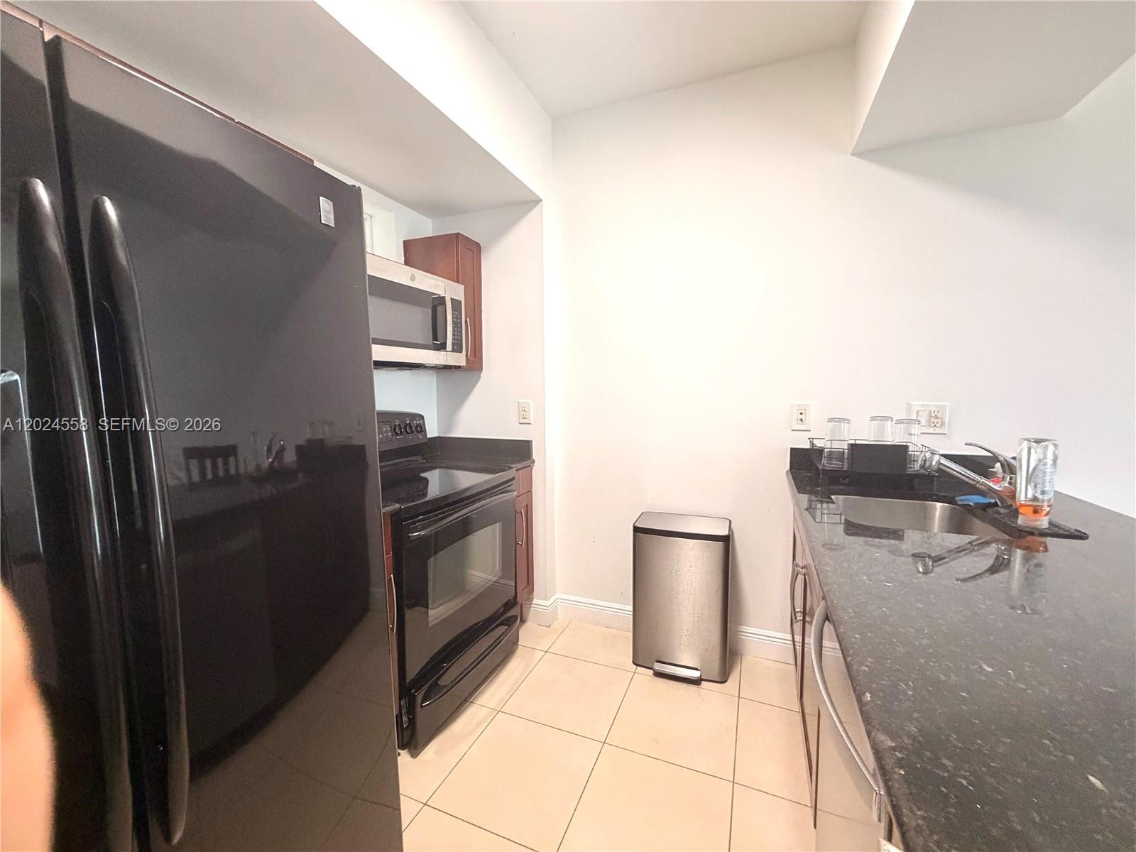 A kitchen features black appliances, dark granite countertops, and light-colored tile flooring — 7290 SW 90th St # 303, Miami FL 33156, MIAMI, FL
