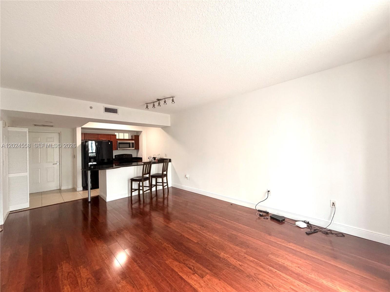 A living room with dark hardwood floors features an open kitchen with a breakfast bar — 7290 SW 90th St # 303, Miami FL 33156, MIAMI, FL